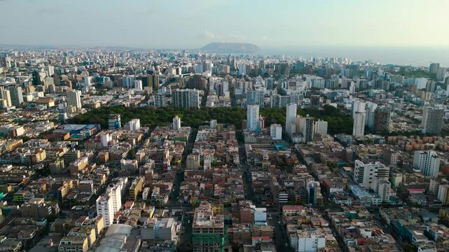 Toma panor&aacute;mica con drone de la ciudad de Lima, con un exuberante parque verde y frondoso en el centro y el mar al fondo, donde se destaca un imponente pe&ntilde;asco, en una tarde de verano tranquilo