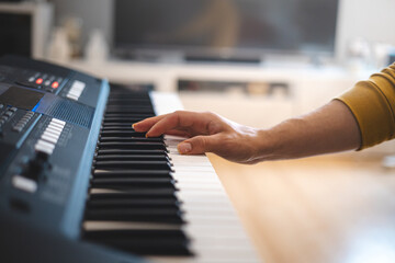 Obraz premium Close-up of hands playing a digital keyboard under warm natural light, capturing the essence of creativity, focus, and musical passion in an intimate indoor setting