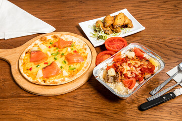 Hawaiian Smoked Salmon Pizza, Lemon honey chicken wings, Spanish baked Pork Chop Rice isolated on wooden table with fork, knife and spoon side view of italian food
