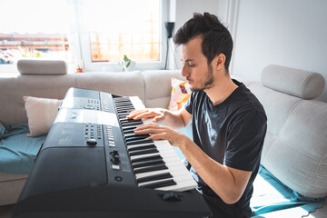 Young musician deeply focused while playing a digital keyboard in a sunlit, modern living room. The...