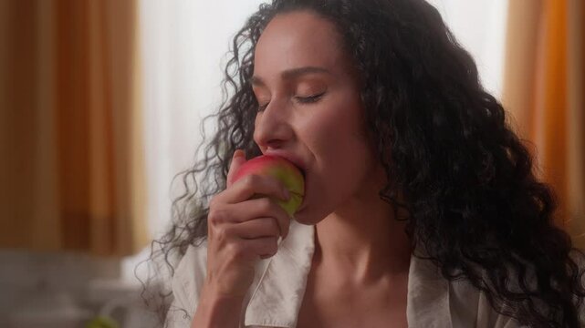 Happy Hispanic Latina girl female lady woman healthy eat food nutrition throwing apple in air catch hand bite fruit at home kitchen smiling at camera chewing eating health care weight control indoors