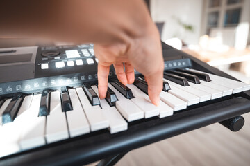 Close-up of a digital keyboard with a hand playing a melody, illuminated by soft natural light. The...