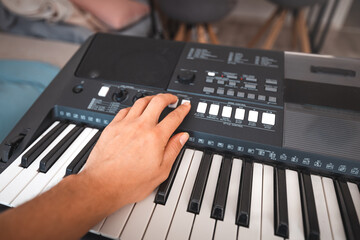 Close-up of a digital keyboard with a hand playing a melody, illuminated by soft natural light. The...