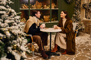 A young couple shares a cozy moment over warm drinks, surrounded by winter decorations and snow.