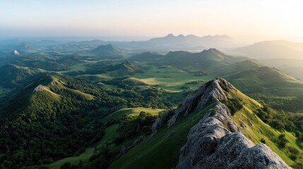 Fototapeta premium Aerial view of lush green mountain range with rocky peaks and valleys under a clear sky at sunrise, showcasing natural landscape and terrain.