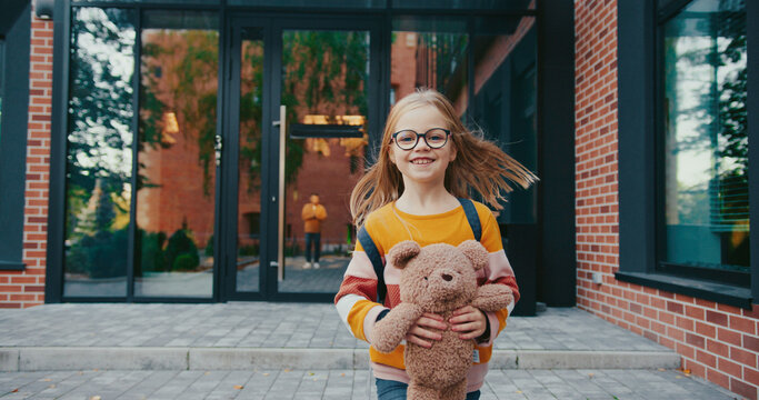 A little girl holding teddy bear while running to the camera. Caring dad expecting his cute daughter outdoors. Warm moment of parenthood. Relationship concept.