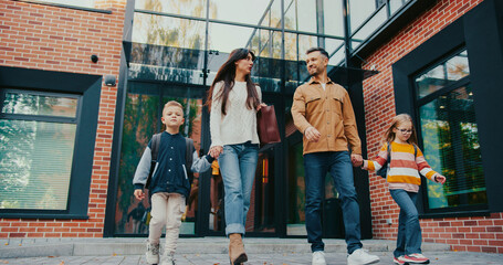 Parents accompanying their children on way back from school. Walking together. Caucasian man talking with woman. Having friendly discussion. Getting to know each other. Female holding handbag.