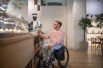 Concentrated disabled man in wheelchair paying for purchase in coffee shop using terminal, credit card. NFC technology, contactless payment, using bonus loyalty system, completing cashless transaction