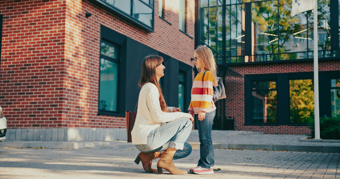 Warm moment of caring Caucasian woman kneeling in front of her daughter. Giving smart advice before first day at new school. Fixing hair of beautiful girl. Busy morning. Trying to be friend.
