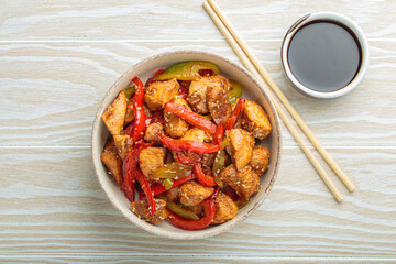 Chicken stir fry with red and green bell peppers sprinkled with sesame seeds, served in bowl, with chopsticks and soy sauce aside, composing a delicious asian meal