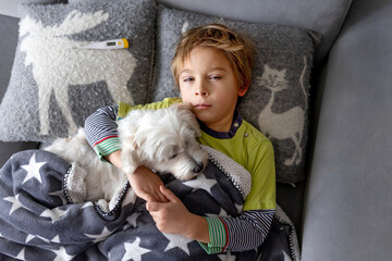 Obraz premium Sick child, preschool boy, lying in bed with a fever, resting at home with his pet dog, mom checking on him