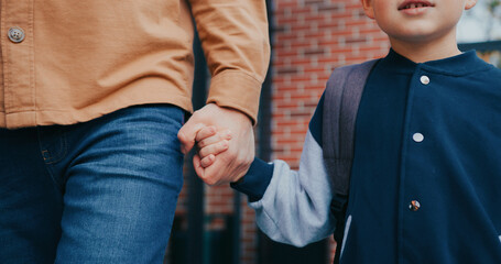 Camera focus on Caucasian boy holding his fathers hand. Walking together from school. Carrying backpack. Protective and supportive parent looking after little kid. Parenthood concept.