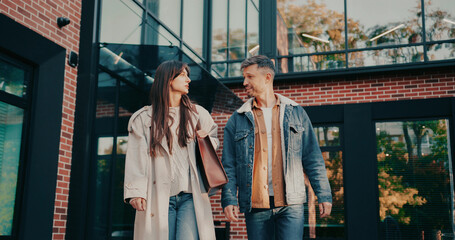 Positive Caucasian couple leaving modern building together. Discussing something on their way to...