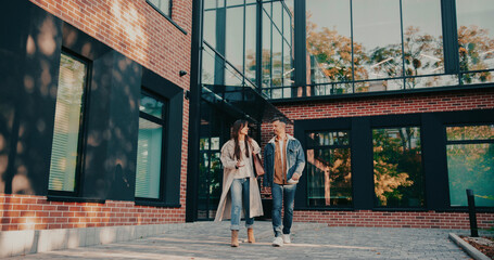 Young teachers leaving school together. Going back home after hard working day. Having active conversation while walking. Talking about plans for evening or weekend. Discussing what happened at work.