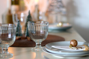 Table set for Christmas meal with plates, glasses, holiday decorations, lit candles and wine. Selective focus.