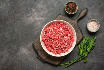 Raw mince beef, ground meat in bowl with spices on wooden cutting board, dark grunge background, top view, flat lay