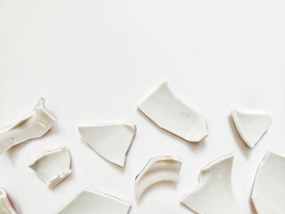 Several broken ceramic pieces scattered on a white surface, symbolizing fragility and destruction.