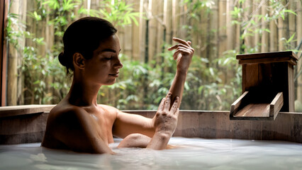 A young woman relaxes in a powdery Japanese bath in a tropical setting. Serene spa experience. Concept of spa, wellness, relaxation and rejuvenation.