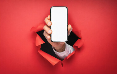 Hand holds a smartphone with white display breaks through a red wall. Concept of message, announce