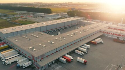 Aerial View of Large Modern Distribution Center with Multiple Loading Docks, Semi Trucks and Freight Terminal Complex at Industrial Area, Sunset Golden Hour