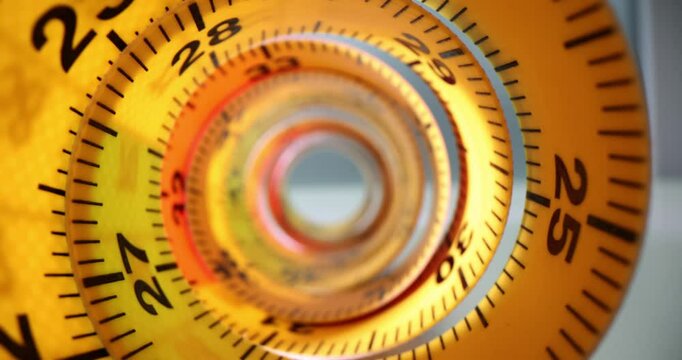 Rolled yellow measuring tape creates tunnel-like effect. Instrument with digits and lines for making accurate measurements placed on table