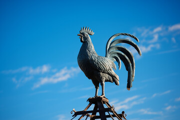 A striking image of a traditional weathercock perched atop a pointed rooftop, silhouetted against a clear blue sky