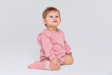 Cute baby girl in a pink princess bodysuit and socks sitting on a white background and looking up at empty copy space. Closeup. Childhood and fashion. Birthday party concept. High quality photo © Irina Mikhailichenko