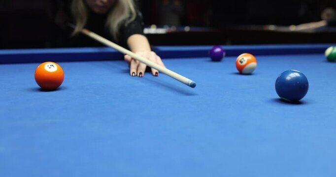 Focused blonde woman billiards player strikes rack using cue ball. Skilled female engages in enjoyable pool game session in club with blue table
