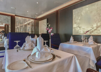 Formal and elegant ocean view dining room restaurant onboard luxury cruiseship or cruise ship liner with set tables in modern Art Deco interior design style and ceiling ambient lighting