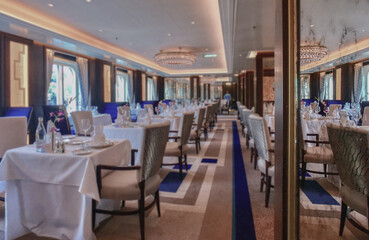 Formal and elegant ocean view dining room restaurant onboard luxury cruiseship or cruise ship liner with set tables in modern Art Deco interior design style and ceiling ambient lighting