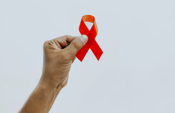 Hand holding Red Ribbon for December World Aids Day (acquired immune deficiency syndrome), multiple myeloma Cancer Awareness month and National Red ribbon week. Healthcare and world cancer day concept