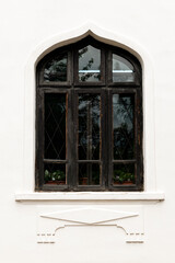 Vintage Arched Window Design. Elegant black arched window with intricate detailing on a white textured wall, reflecting surrounding greenery and sky, showcasing a timeless architectural style.