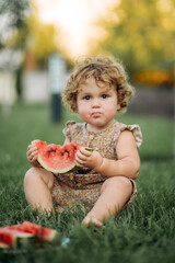 Adorable little girl eating watermelon sitting on the grass in the park