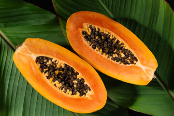 Juicy papaya fruit cut in half, with seeds and bright orange flesh top view. This photo highlights...