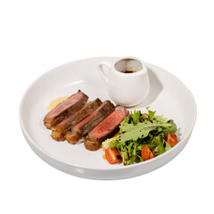 A beautifully plated dish featuring sliced steak, a side salad with tomatoes, and a small gravy boat.