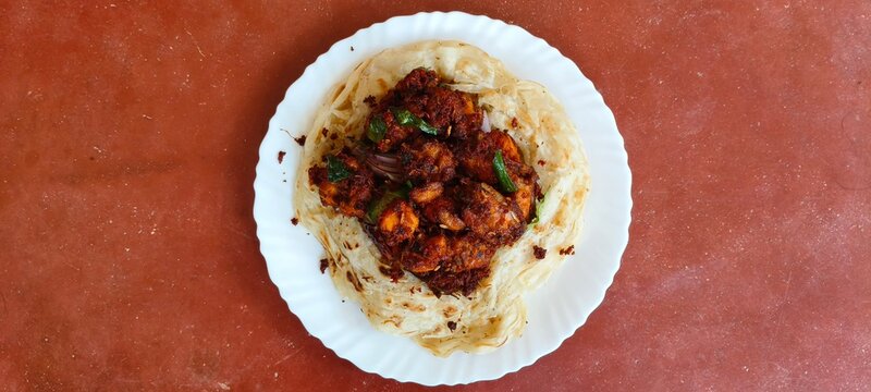 Popular Kerala or malabari south indian dish maida flour porotta, paratha or roti with spicy fried chicken 65 curry on plate isolated on table with copy space. Beautiful Indian food closeup top view.