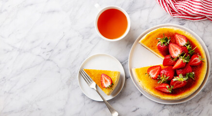 Cheesecake dessert with fresh strawberries and cup of tea. Marble background. Copy space. Top view.