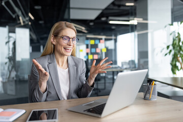 Mature woman businesswoman excitedly interacts during online meeting through laptop in modern...