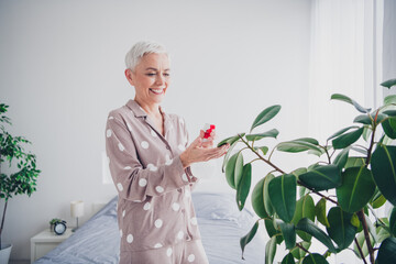 Elderly woman enjoying morning in pajamas with vibrant plants in bright bedroom