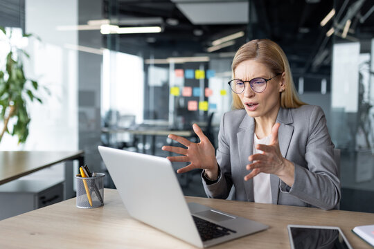 Mature woman businesswoman sitting in office looking frustrated at laptop. Expresses stress and confusion over work project or technical issue.