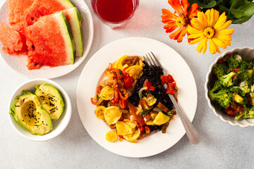 A filling breakfast of black rice with stewed tomatoes, zucchini, peppers, and onions, accompanied by a fresh salad of tomatoes, broccoli, radish, and avocado