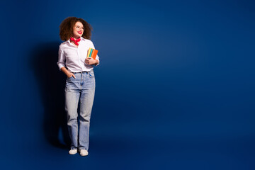 Full length photo of adorable lovely girl wear red tied handkerchief holding book stack looking empty space isolated blue color background