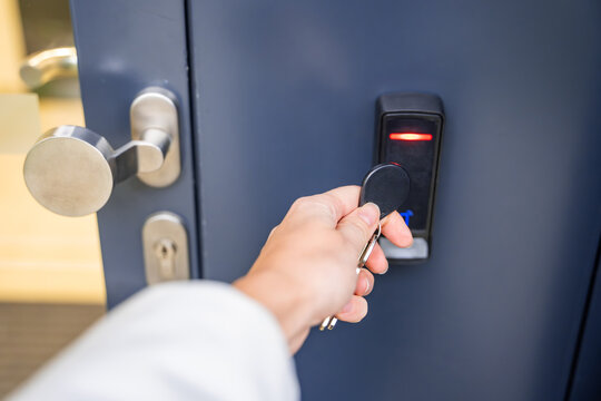 Close up view of person using a electric lock key fob to access a building via a reader of entry system mounted on a house wall