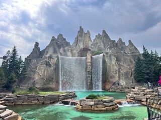 Artificial Mountain Waterfall with Pool in a Theme Park Under a Cloudy Sky