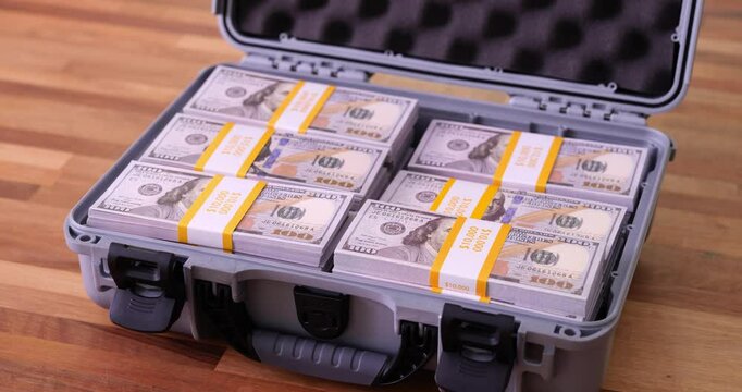 Stacks of U.S. dollars filling up plastic container on wooden surface. Plastic briefcase loaded with bundles of foreign currency banknotes