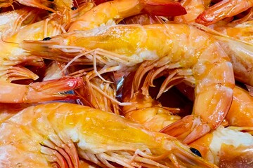 Cooked shrimp, which should be steamed or boiled. Ready-to-eat food, as can be identified by the bright orange shell and shiny appearance. The shrimp are arranged closely together.