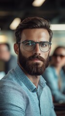 Obraz premium A bearded man wearing glasses and a blue shirt is captured, presenting a modern and intellectual appearance in an ambient setting, exuding confidence and style.