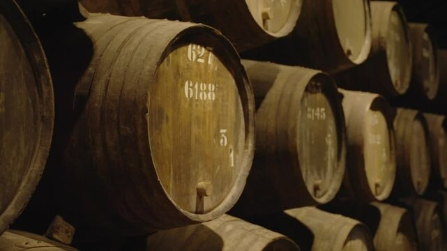 Stack of oak wine barrels with labels and tags for aging and storage in winery. Special conditions indoors in dark and cold cellar in Porto Portugal. Winemaking process business in underground store