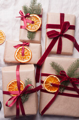 Wrapped gifts with dried orange and velvet pine branches and bows on white linen Christmas decoration diy recipe copy space flat lay top view holiday inspiration