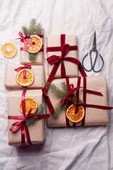 Wrapped gifts with dried orange and velvet pine branches and bows on white linen Christmas decoration diy recipe copy space flat lay top view holiday inspiration